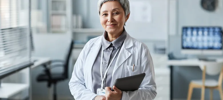 happy-mature-female-doctor-with-tablet-standing-front-camera